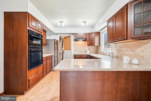 kitchen with a peninsula, under cabinet range hood, high quality fridge, and glass insert cabinets