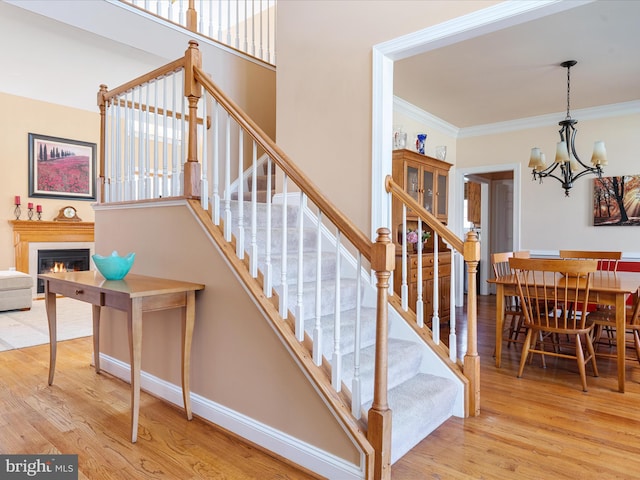 stairway featuring a warm lit fireplace, baseboards, ornamental molding, and wood finished floors