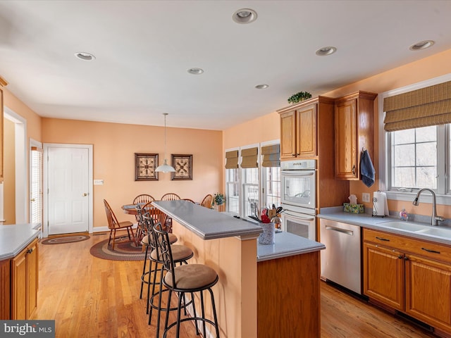 kitchen with light wood finished floors, stainless steel dishwasher, double oven, a sink, and a kitchen bar