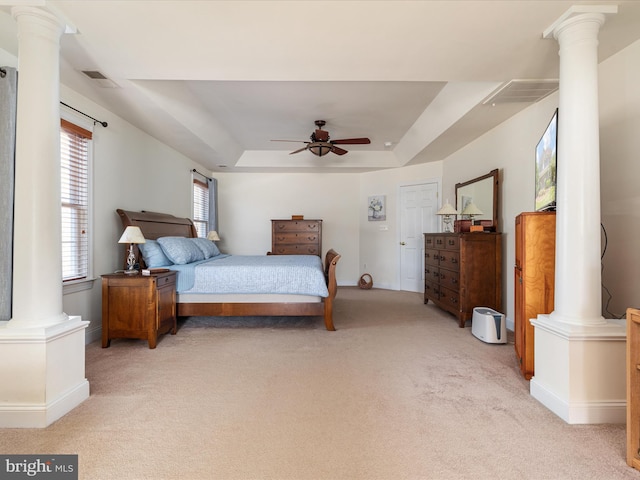 bedroom with light colored carpet, visible vents, a ceiling fan, a tray ceiling, and ornate columns