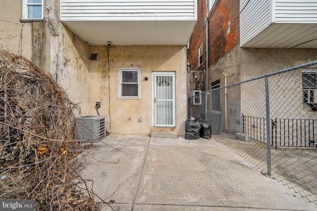 view of exterior entry featuring cooling unit, a patio area, fence, and stucco siding