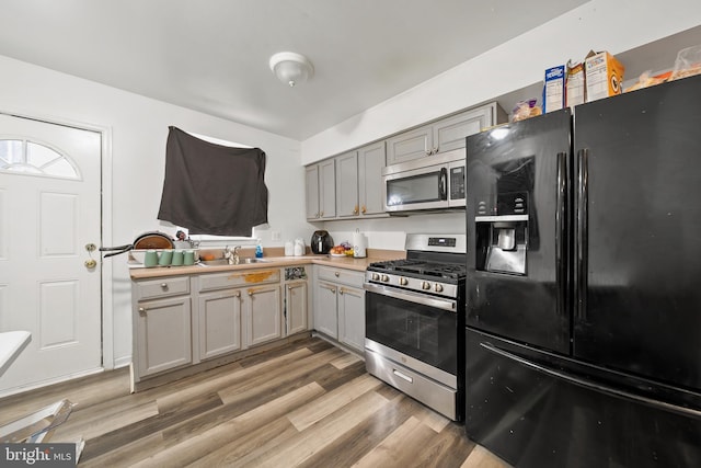 kitchen with light wood finished floors, appliances with stainless steel finishes, gray cabinets, and a sink