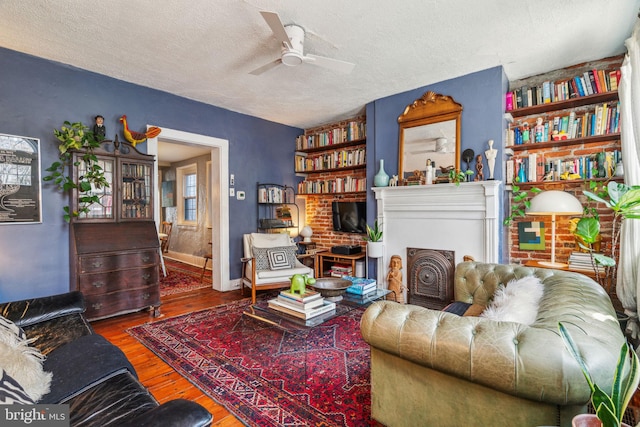 living room with a textured ceiling, ceiling fan, a fireplace, and wood finished floors