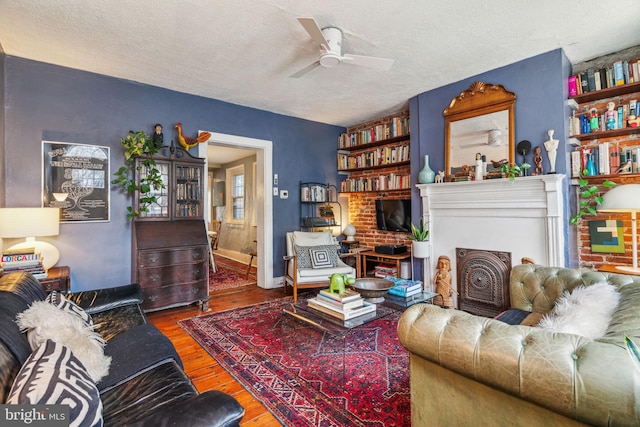 living area with a textured ceiling, a ceiling fan, a fireplace, and wood finished floors