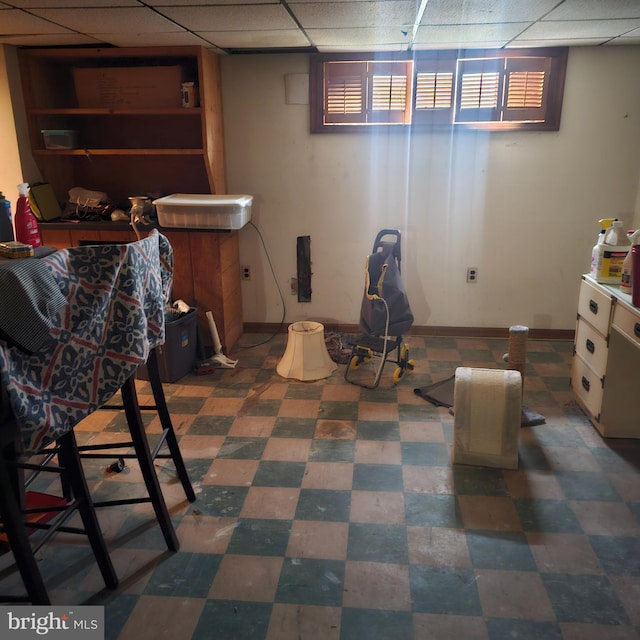 basement featuring baseboards, a drop ceiling, and tile patterned floors