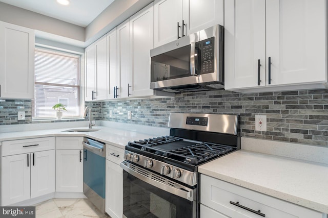 kitchen featuring white cabinets, appliances with stainless steel finishes, a sink, marble finish floor, and backsplash