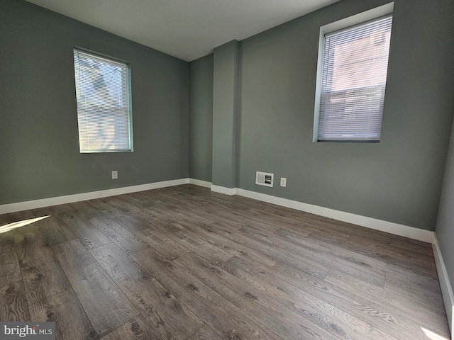 spare room with wood finished floors, visible vents, and baseboards