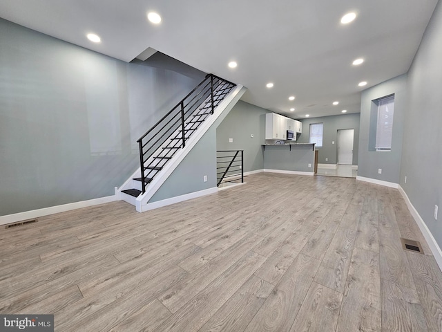 unfurnished living room featuring light wood-type flooring, stairway, visible vents, and recessed lighting