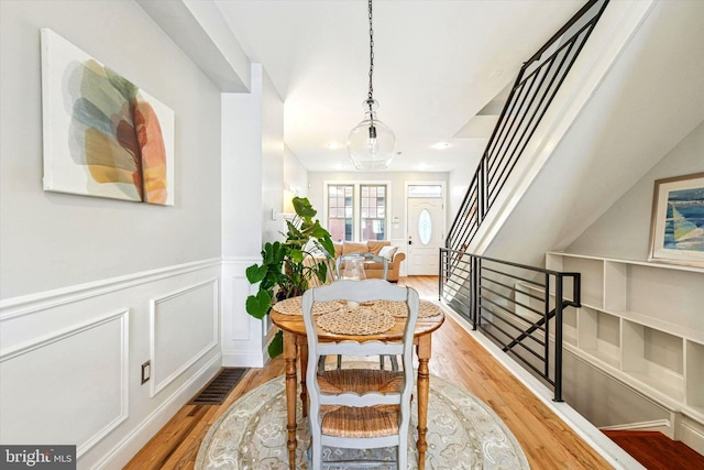 dining room with visible vents, a wainscoted wall, stairs, wood finished floors, and a decorative wall