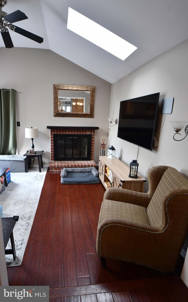 living room with ceiling fan, vaulted ceiling with skylight, a fireplace, and wood-type flooring