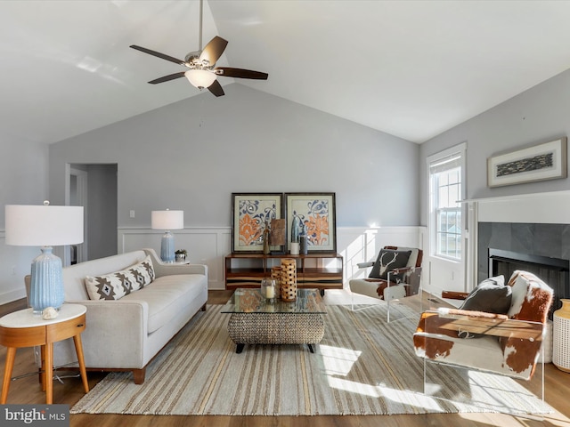 living area with lofted ceiling, ceiling fan, a tile fireplace, wood finished floors, and wainscoting