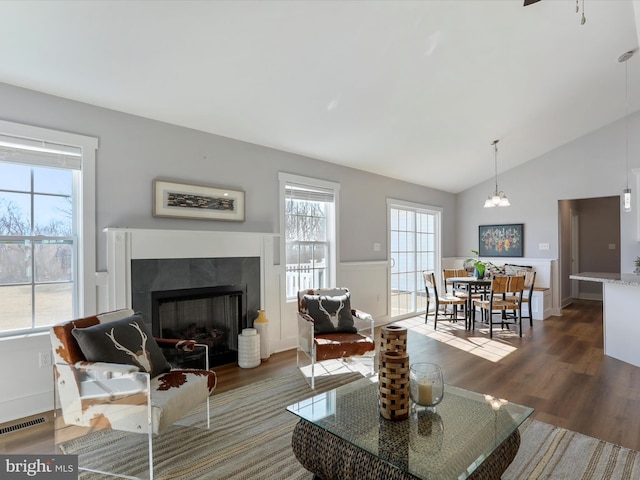 living area with lofted ceiling, a wainscoted wall, a fireplace, wood finished floors, and visible vents