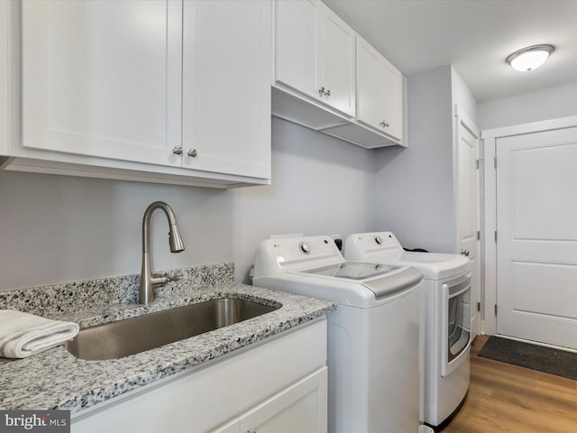 laundry room featuring wood finished floors, a sink, cabinet space, and washer and dryer