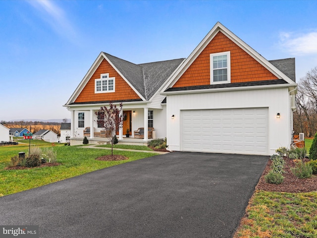 view of front facade featuring covered porch, aphalt driveway, a front yard, and an attached garage