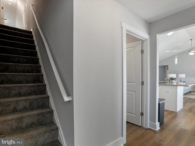 staircase featuring a ceiling fan, vaulted ceiling, and wood finished floors