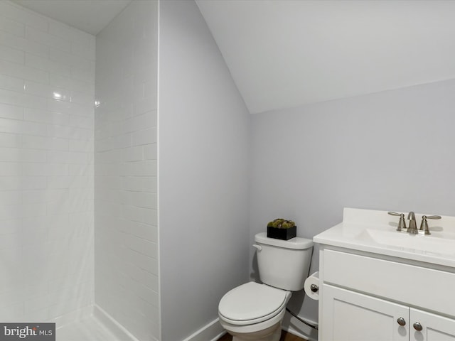 bathroom featuring lofted ceiling, toilet, vanity, baseboards, and tiled shower