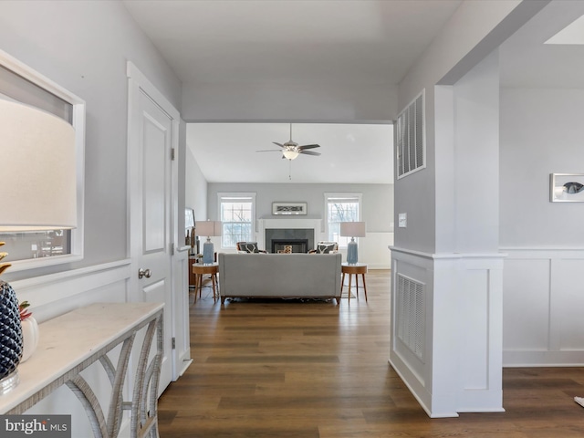 hall with dark wood-type flooring, wainscoting, visible vents, and a decorative wall