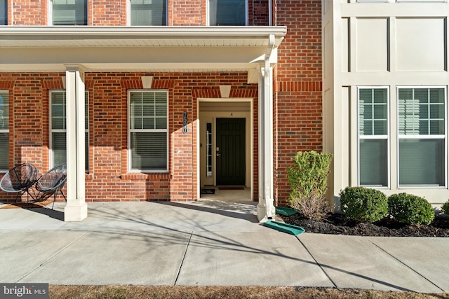 doorway to property featuring a porch and brick siding