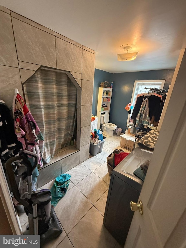 bathroom featuring toilet, washer / dryer, tile patterned flooring, and a tile fireplace