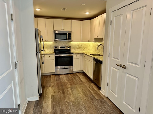 kitchen featuring light stone counters, dark wood-style flooring, stainless steel appliances, backsplash, and a sink