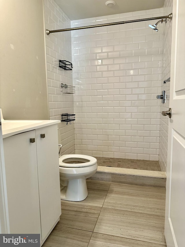 bathroom featuring toilet, tiled shower, and vanity