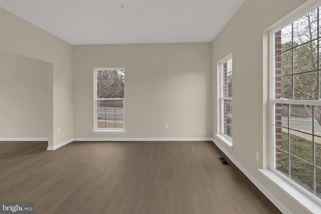 unfurnished room with dark wood-style floors, a wealth of natural light, and visible vents