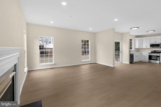 unfurnished living room with baseboards, wood finished floors, a fireplace with flush hearth, and recessed lighting