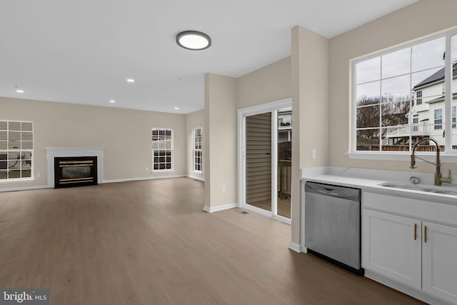 kitchen with a sink, white cabinets, open floor plan, light countertops, and dishwasher