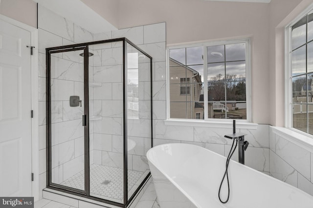 bathroom with marble finish floor, a shower stall, tile walls, and a freestanding bath