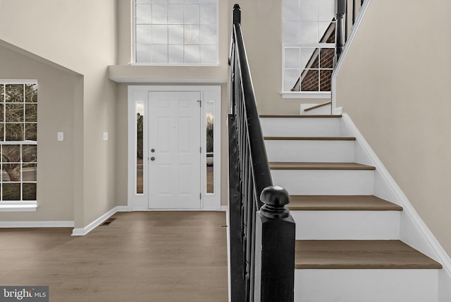 foyer entrance with wood finished floors, visible vents, a towering ceiling, stairs, and baseboards