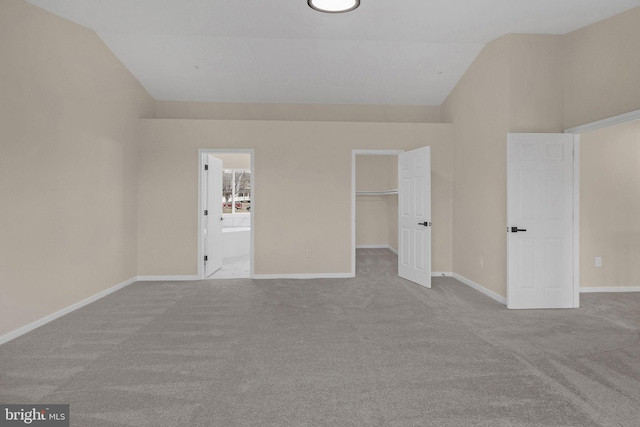 unfurnished bedroom with lofted ceiling, light colored carpet, a spacious closet, ensuite bathroom, and baseboards