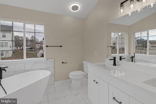 full bath with marble finish floor, double vanity, lofted ceiling, a freestanding bath, and a sink