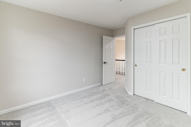 unfurnished bedroom with a closet, light carpet, and baseboards