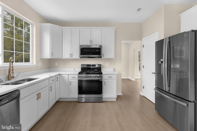 kitchen featuring stainless steel appliances, light countertops, light wood-style flooring, white cabinetry, and a sink