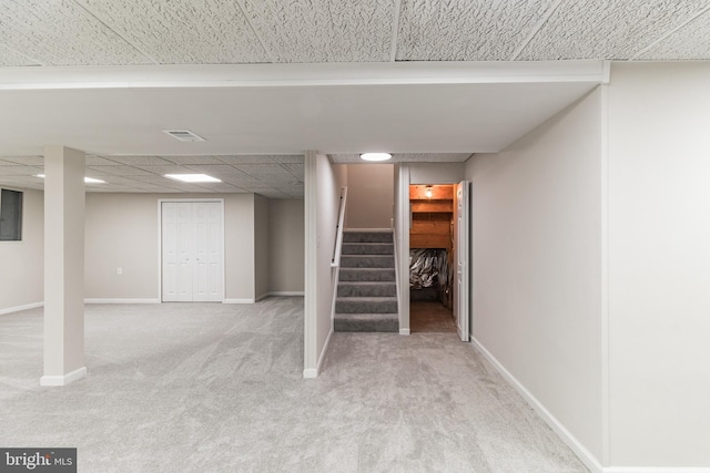 finished basement with light colored carpet, a drop ceiling, baseboards, and stairs