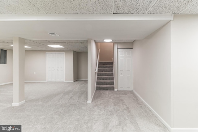 finished basement with a drop ceiling, light carpet, visible vents, baseboards, and stairway