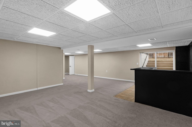 finished below grade area featuring a paneled ceiling, visible vents, baseboards, stairs, and carpet