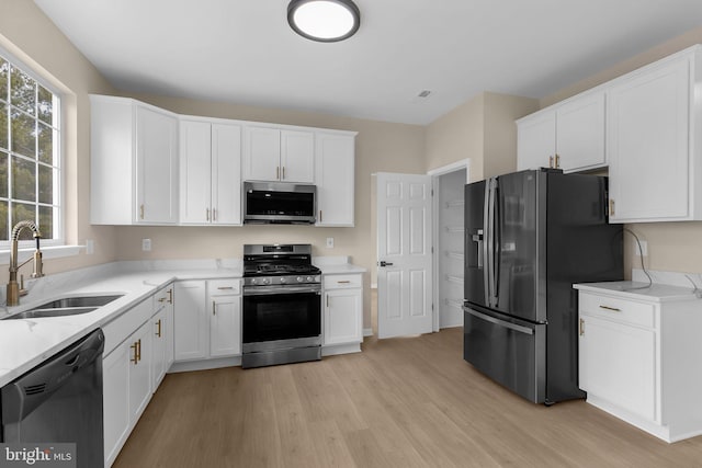 kitchen with stainless steel appliances, white cabinets, a sink, and light wood finished floors