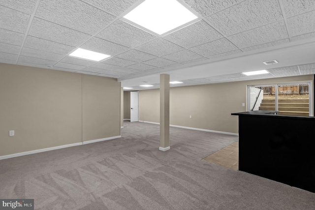 below grade area with baseboards, visible vents, a drop ceiling, and carpet flooring