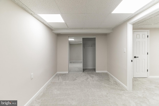 unfurnished bedroom with a closet, light colored carpet, a drop ceiling, and baseboards