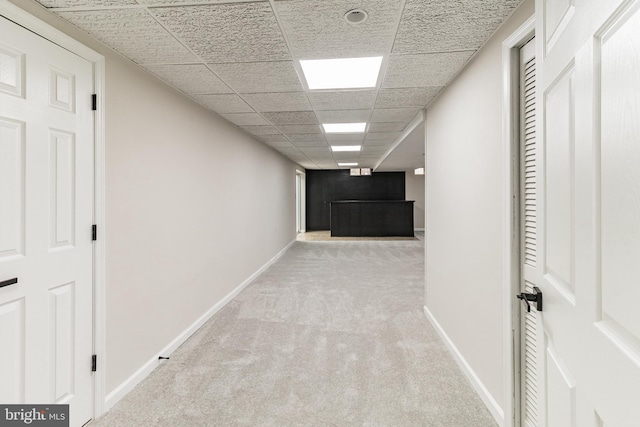 hall with light carpet, baseboards, and a paneled ceiling