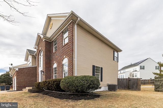 view of property exterior featuring brick siding, fence, a lawn, and central AC unit