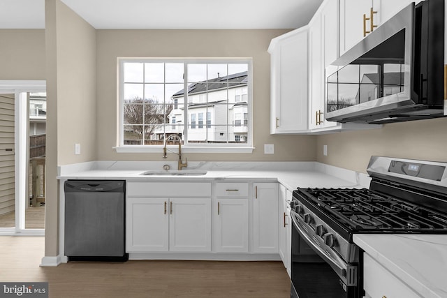 kitchen with appliances with stainless steel finishes, light wood-type flooring, white cabinets, and a sink