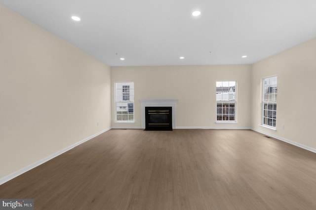 unfurnished living room featuring wood finished floors, recessed lighting, a fireplace with flush hearth, and baseboards