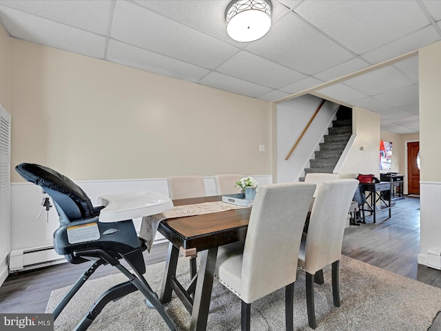 dining room featuring a paneled ceiling, a baseboard heating unit, stairway, and dark wood-style flooring