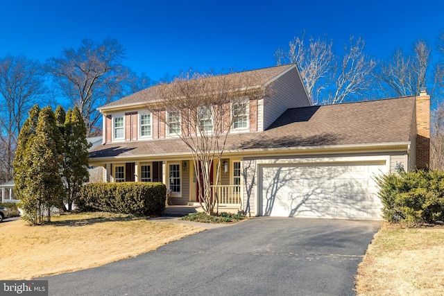 colonial house featuring an attached garage, covered porch, a shingled roof, a chimney, and aphalt driveway