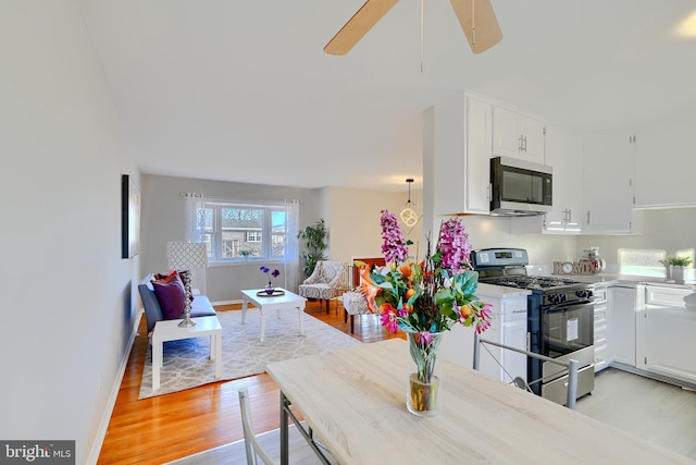 kitchen featuring range with gas cooktop, stainless steel microwave, light wood finished floors, and white cabinets