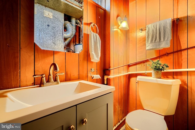 half bathroom featuring toilet, wood walls, and vanity