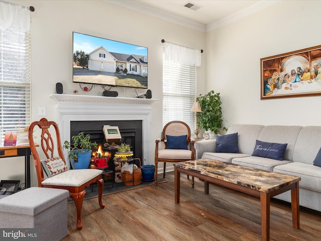 living room featuring a warm lit fireplace, crown molding, visible vents, and wood finished floors