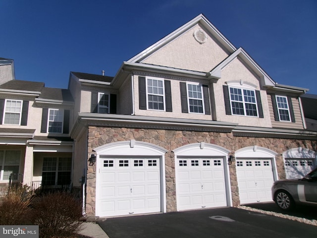 view of front of home featuring a garage, stone siding, aphalt driveway, and stucco siding